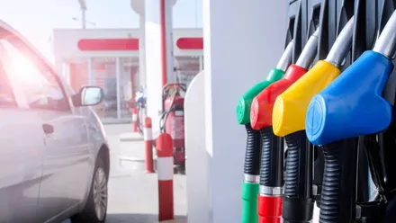 imagem de um carro popular de cor cinza ao lado de uma bomba de combustíveis em um posto de gasolina