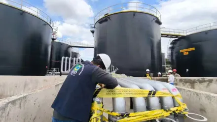 Técnico realizando inspeção em dutos de combustível em base de armazenamento com tanques industriais