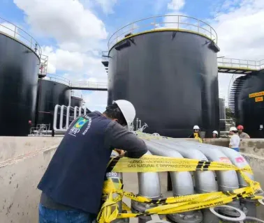 Técnico realizando inspeção em dutos de combustível em base de armazenamento com tanques industriais
