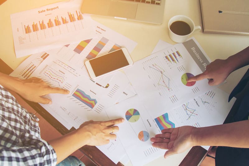 Pessoas analisando gráficos e dados em folhas de papel para implementar estratégias de marketing nos postos.